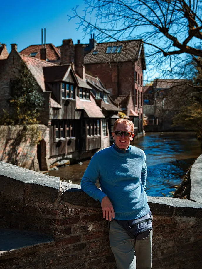 Diego posando junto al canal medieval de Brujas con edificios históricos de fondo