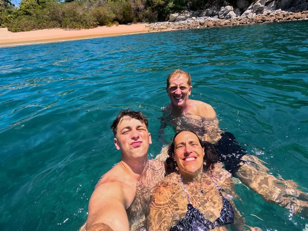 Tres personas en el agua transparente de una bahía aislada de Huatulco con arena blanca al fondo