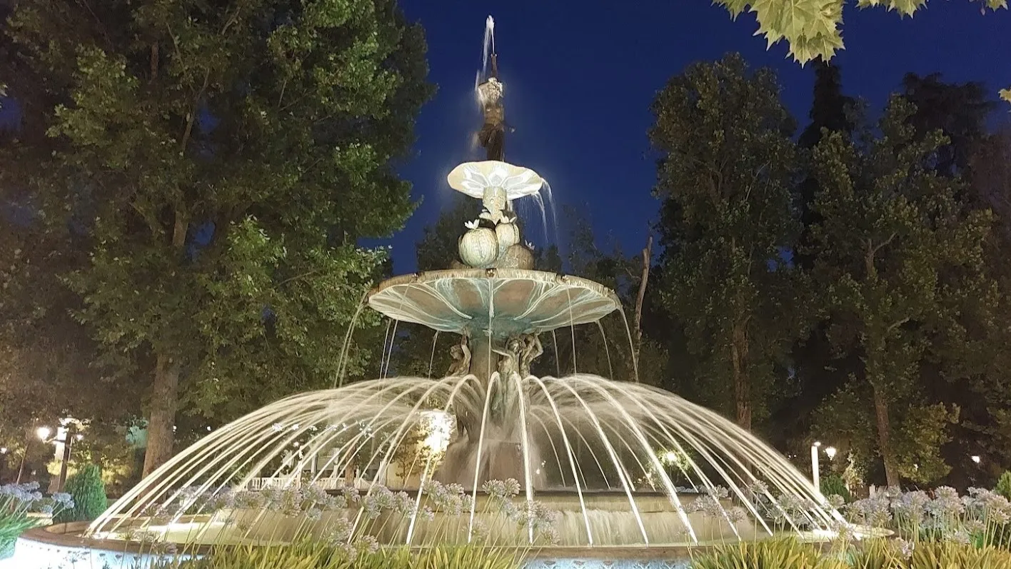 Fuente monumental de Granada iluminada de noche entre árboles