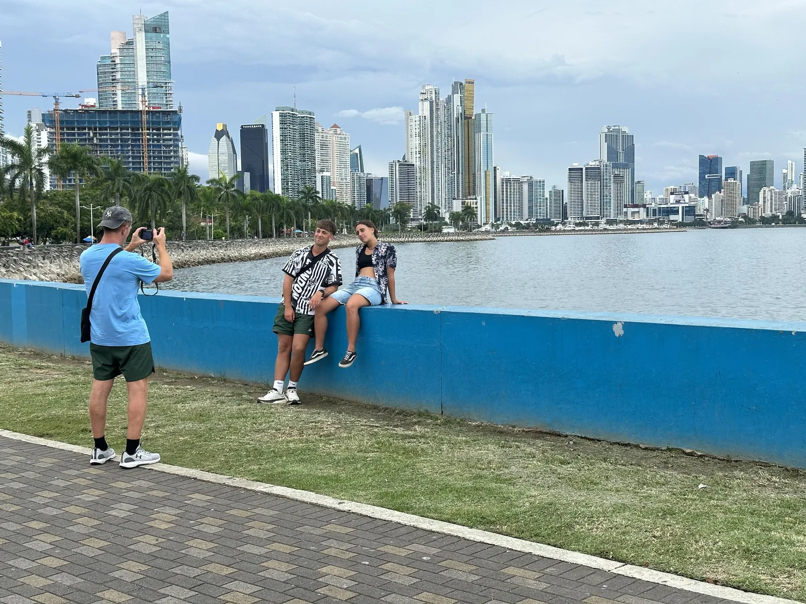 Agus y Agustina sentados sobre el muro azul de la Cinta Costera con el skyline de rascacielos de fondo