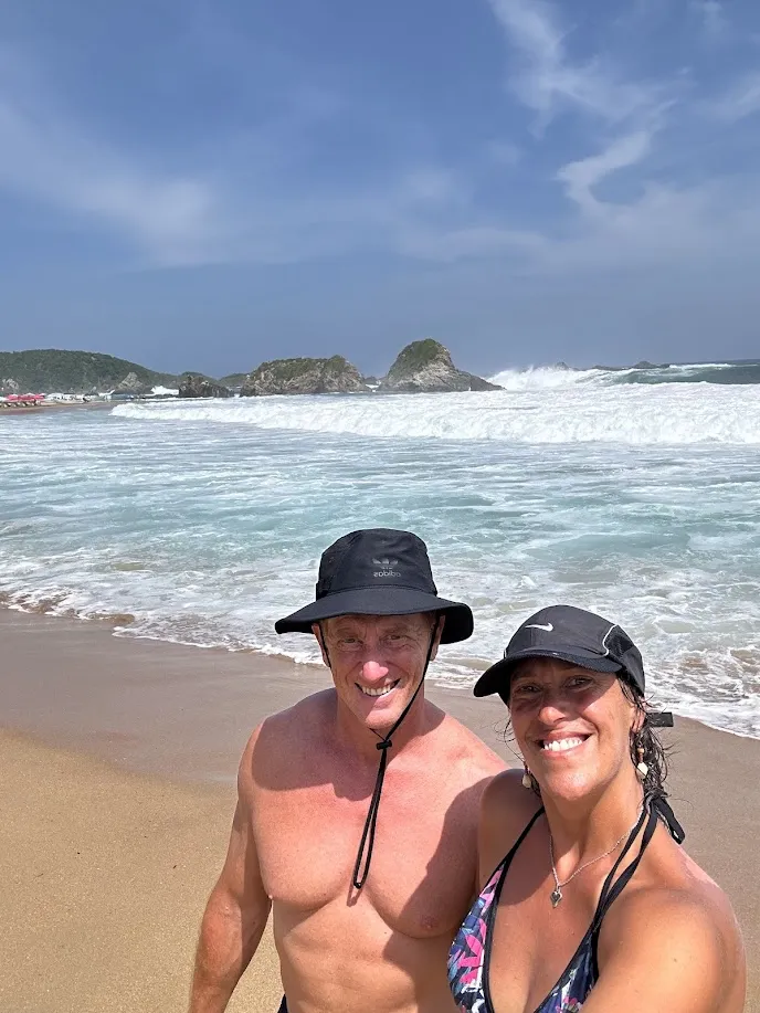 La pareja en San Agustinillo con las imponentes olas del Pacífico y los islotes de fondo