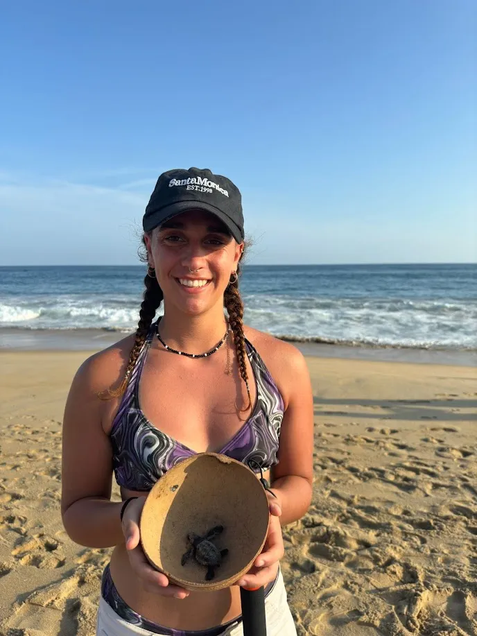 Agus con una tortuguita bebé en la mano en la playa de Puerto Escondido al atardecer
