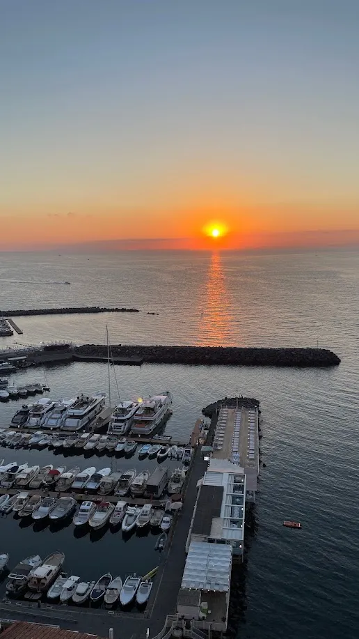 Atardecer de fuego sobre el puerto de Sorrento con yates amarrados y el sol hundiéndose en el mar