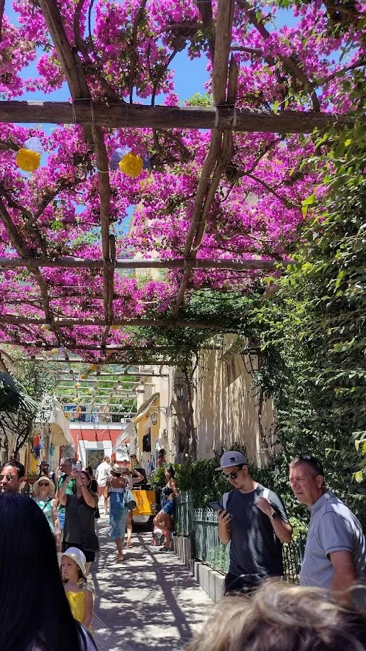Calle de Positano cubierta por una pérgola de buganvillas rosas con peatones caminando