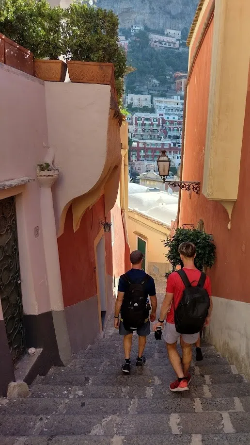 Dos personas bajando por las escalinatas coloridas de Positano entre casas rosas y amarillas