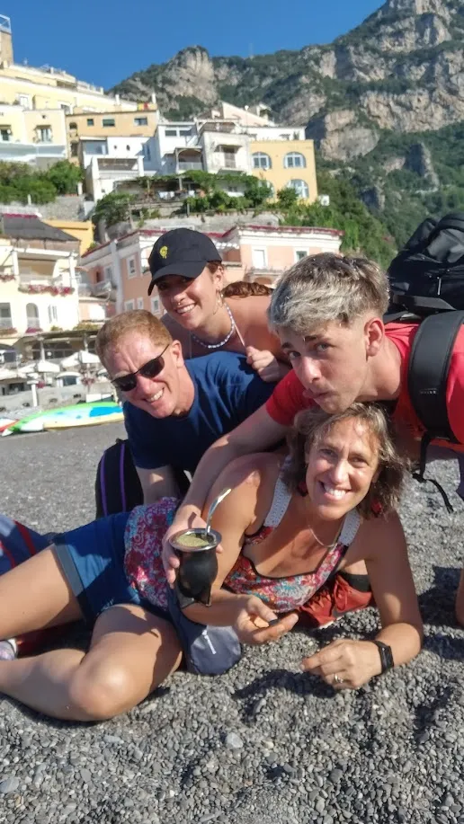 La familia apilada y riendo en la playa de Positano con el mate en mano