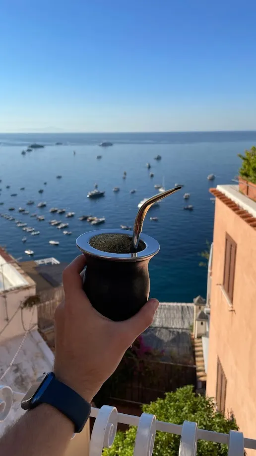 Un mate sostenido frente al mar de Positano con embarcaciones de fondo